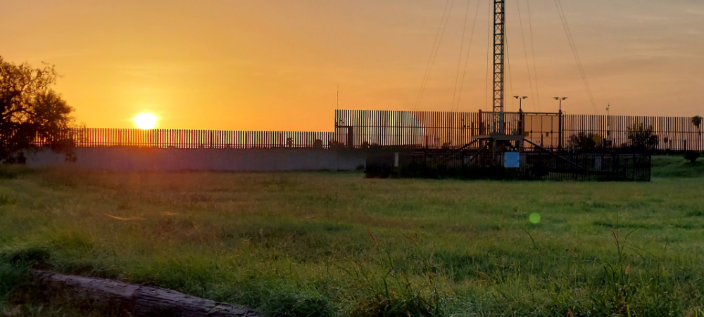 20240719_070610 a fence and grass field with a sunrise