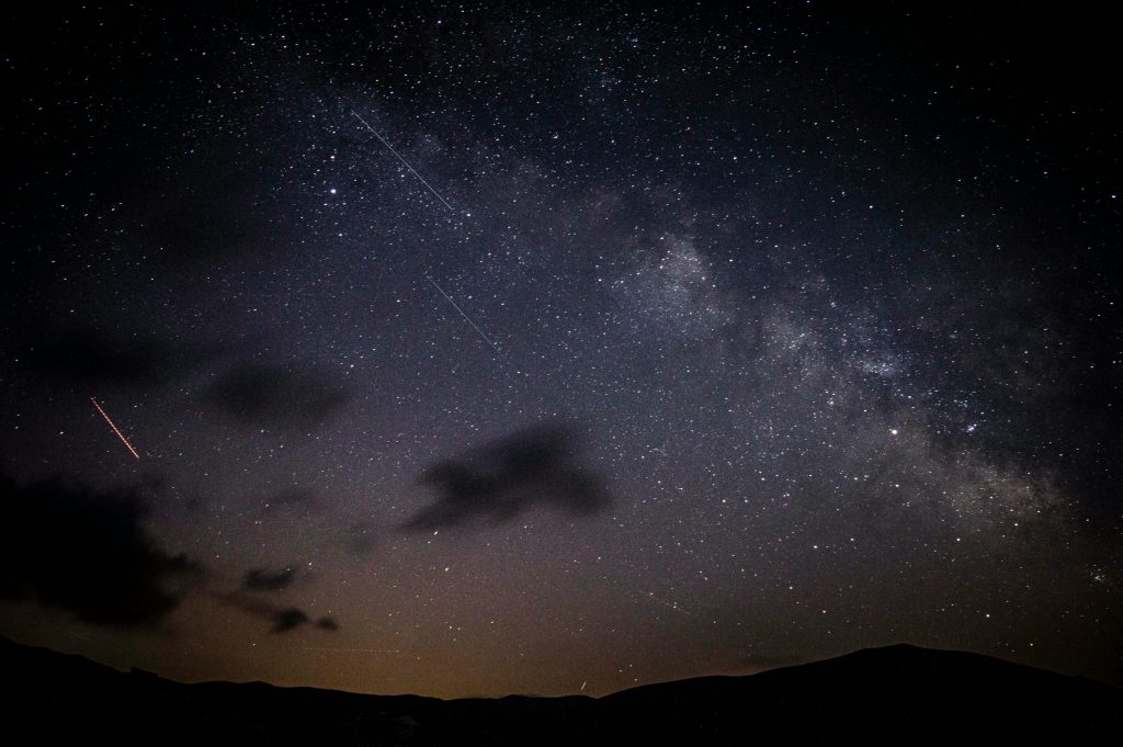 A stunning night sky showcasing stars, clouds, and the Milky Way galaxy with a visible meteor shower.