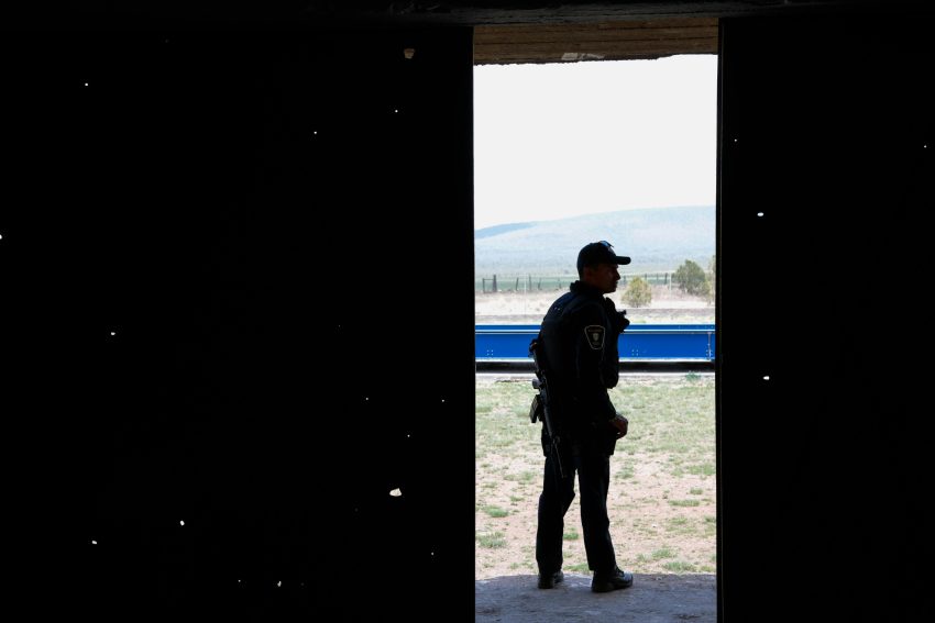 Silhouetted police officer in uniform stands in doorway with a scenic outdoor background.
