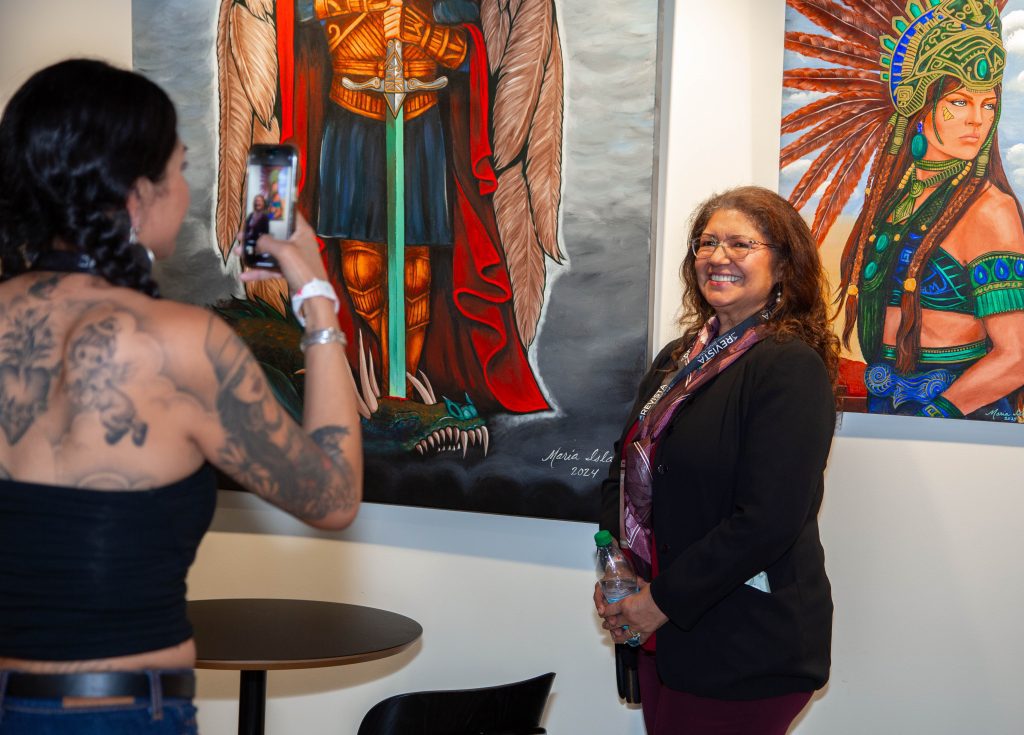 Mujer toma una foto a otra, atrás pinturas