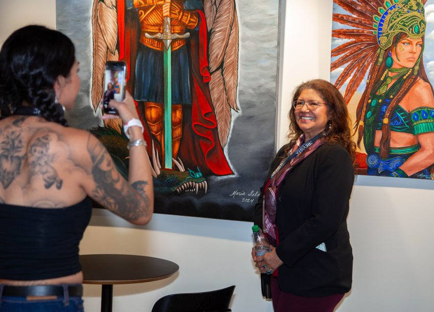 Mujer toma una foto a otra, atrás pinturas